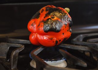 A red pepper cooking over a gas stove flame