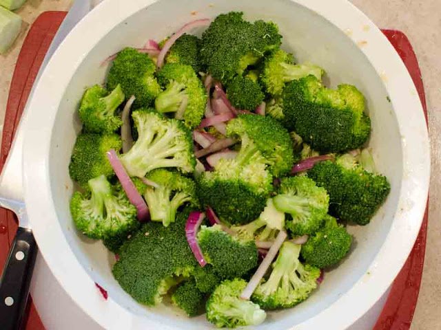 Mixing bowl with broccoli and onions tossed in olive oil