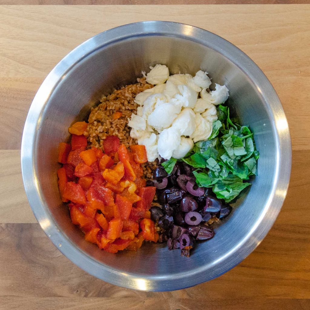 Mixing bowl with wheat berries, roasted red pepper, black olives, mozzarella and basil