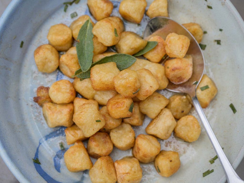 Serving bowl with cauliflower gnocchi tossed in brown butter with fresh sage
